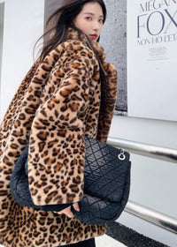 Back view of a woman wearing a luxurious leopard print faux fur coat and carrying a large black quilted denim shoulder bag.