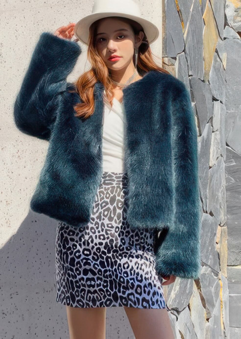 Close-up of a stylish teal blue faux fur jacket paired with a white fedora and rhinestone jewelry for a luxury winter look.
