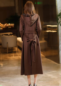 Back view of a long chocolate brown hooded trench coat featuring a cinched waist with a decorative bow-tied belt.