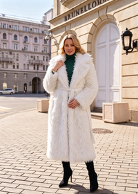 Full-length street style view of a woman wearing an ivory plush faux fur coat belted over an emerald green turtleneck dress with black boots.