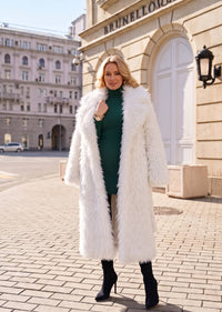 Open-front styling of a plush white faux fur maxi coat worn over a dark green ribbed knit dress.