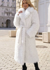 Blonde model wearing a winter white long faux fur wrap coat with notch lapels and self-tie belt, standing on a city street.
