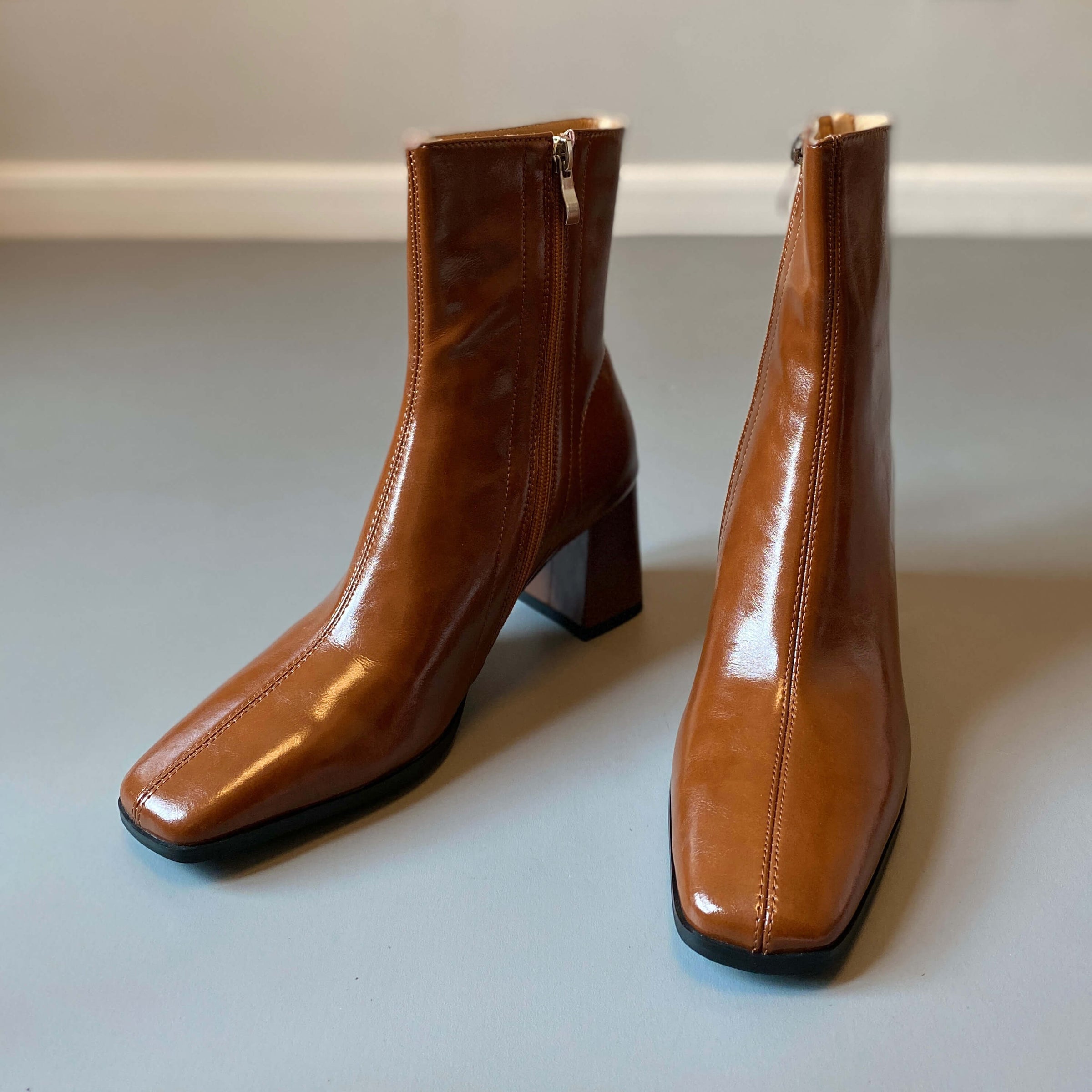 A side-angle view of the tan leather boots, highlighting the side zipper closure and the structured block heel.