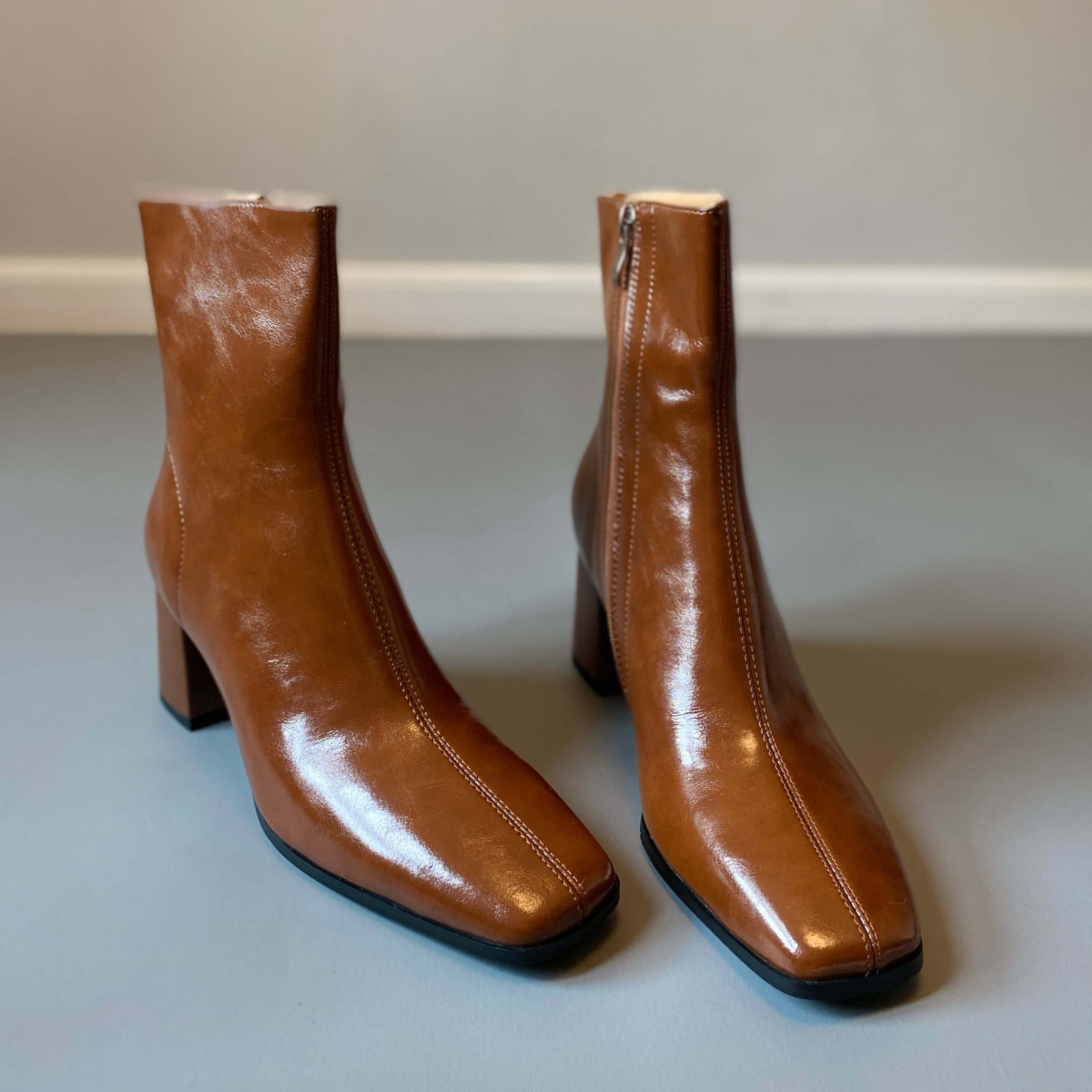 A pair of tan or cognac-colored leather ankle boots with a square toe and a block heel, shown in a front-facing studio shot.