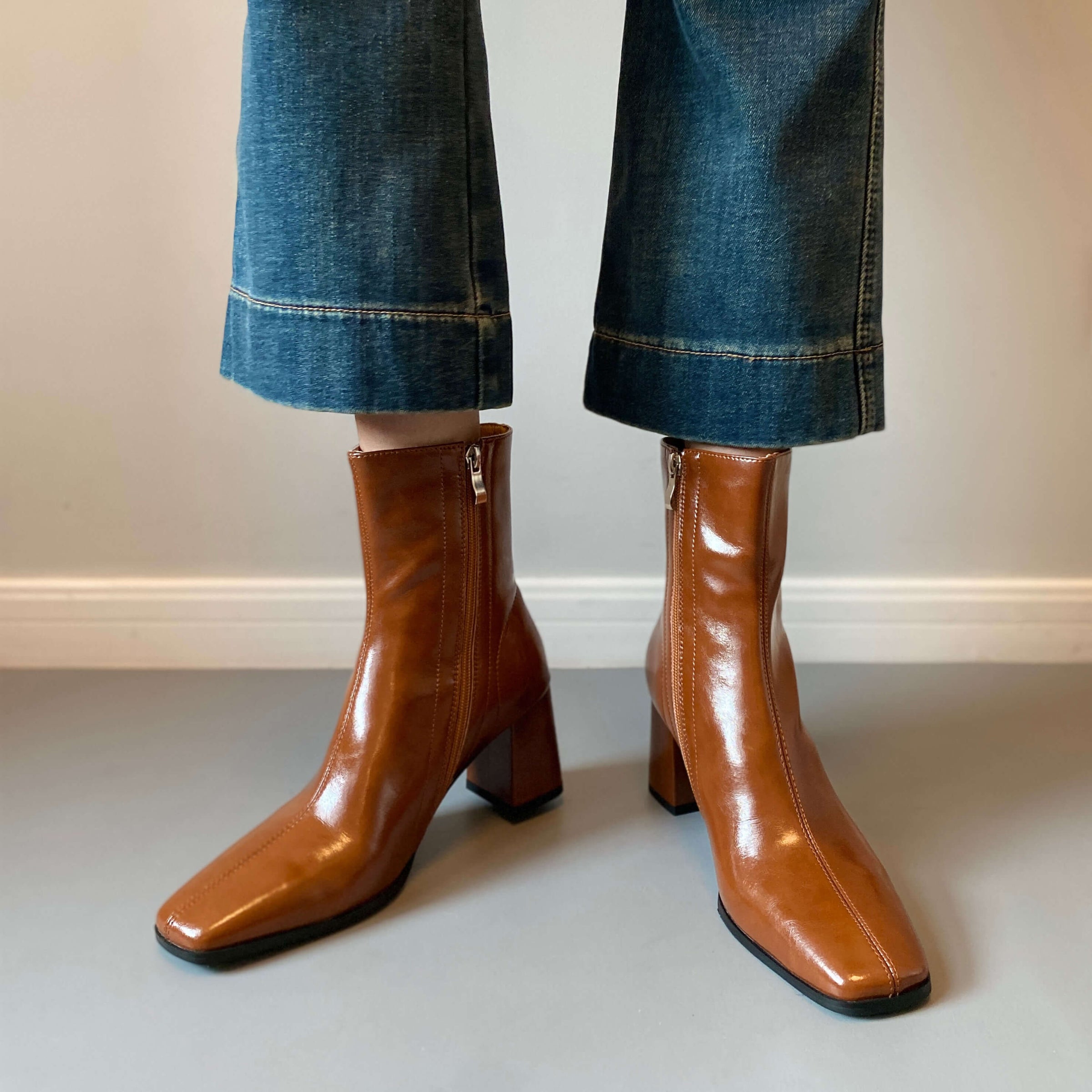 A front-facing view of the tan boots being worn with cropped denim, emphasizing the sleek silhouette of the square toe.