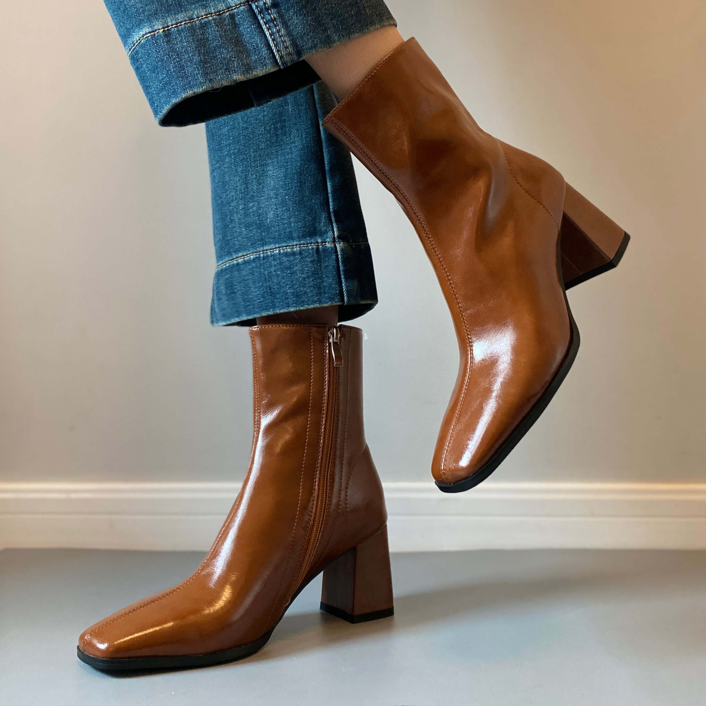 A woman posing in the tan boots with one foot lifted, showcasing the profile of the boot and the height of the block heel.