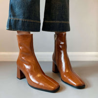 A woman wearing the tan square-toe boots paired with wide-leg blue jeans, showing how the boots fit around the ankle.