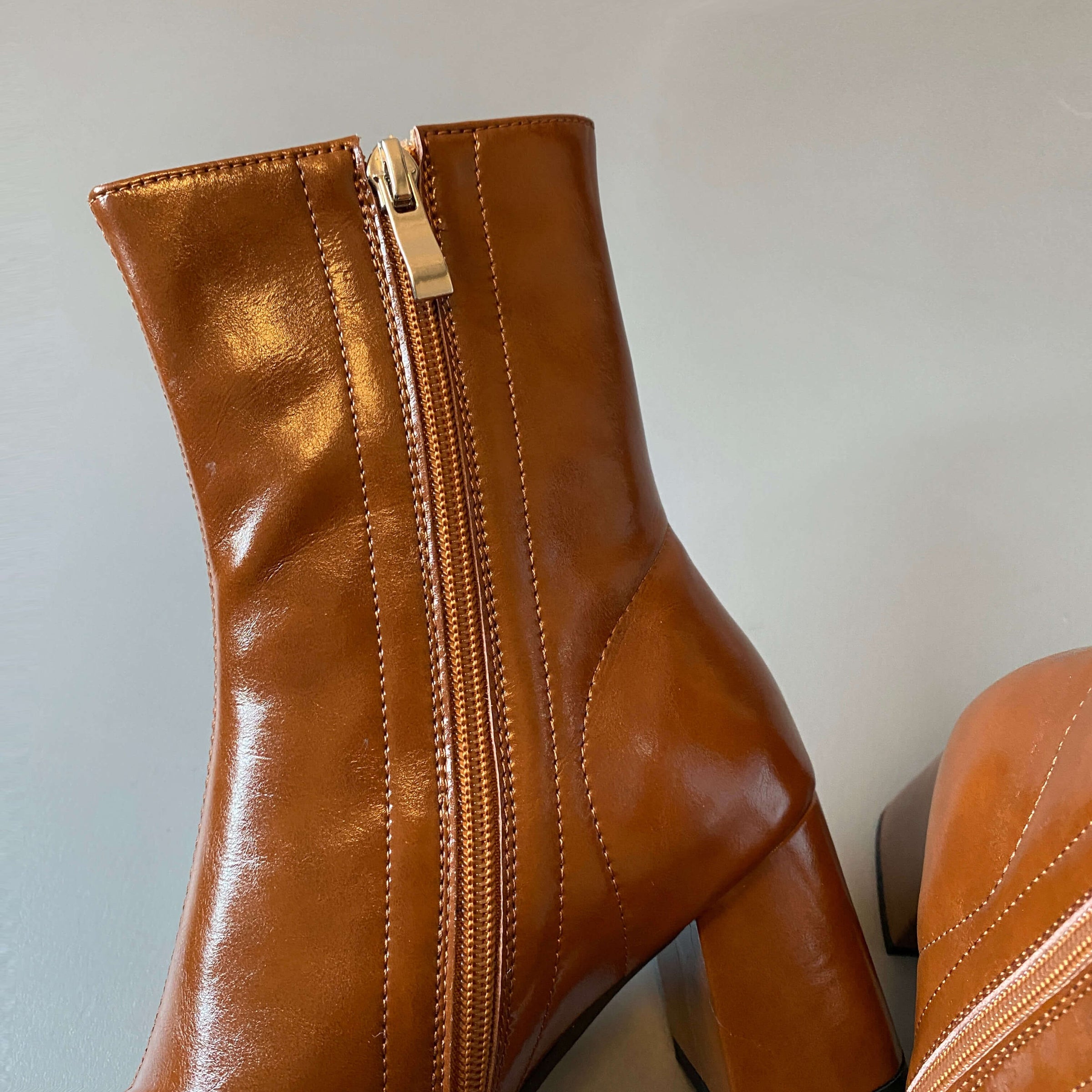 A close-up of the inner side of the tan boot, showing the metallic silver zipper and the neat stitching along the seams.
