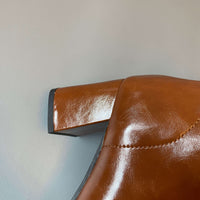 A detailed macro shot of the block heel on the tan leather boot, showing the texture of the material and the black rubber sole at the base.