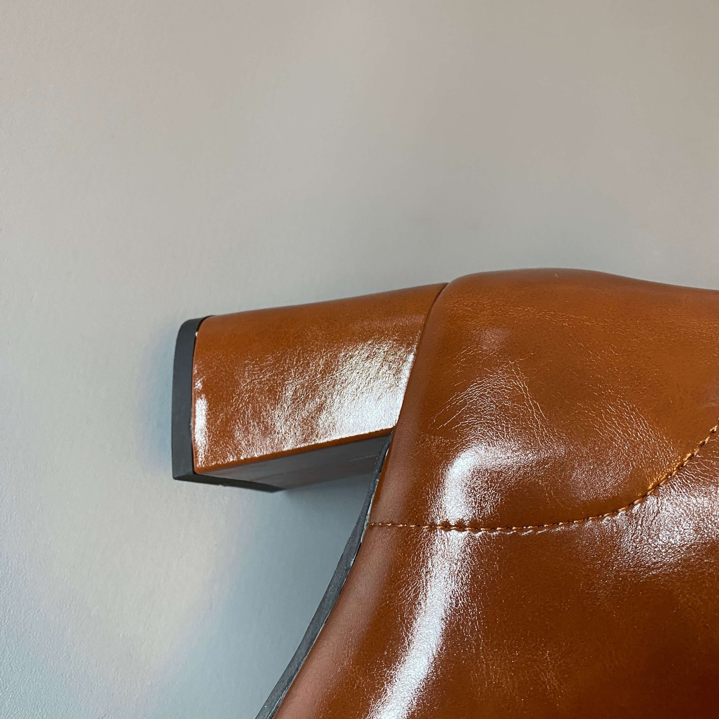 A detailed macro shot of the block heel on the tan leather boot, showing the texture of the material and the black rubber sole at the base.