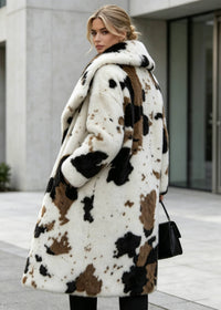 Over-the-shoulder rear view of a blonde model wearing an abstract brown and black cow print faux fur long coat carrying a black leather handbag.
