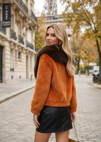 Side back view of woman wearing orange plush faux fur jacket with dark brown fur collar