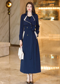 A full-length portrait of the Vivian Seven navy blue trench coat, highlighting the double-breasted button closure and contrast trim, paired with metallic heels and a white luxury purse.