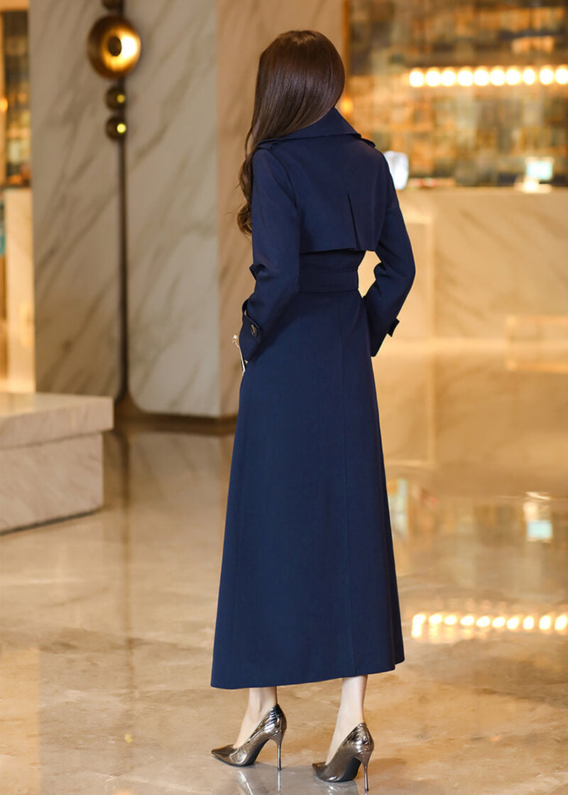 Rear view of the Vivian Seven women’s long trench coat, showcasing the clean lines, back storm flap (gun flap) detail, and the sweeping length of the navy blue fabric.