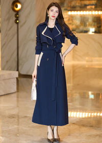Front view of the Vivian Seven long trench coat in navy blue with cream contrast detailing on the pockets and lapels. The coat is belted, showing a slim fit and sophisticated high-end fashion style.