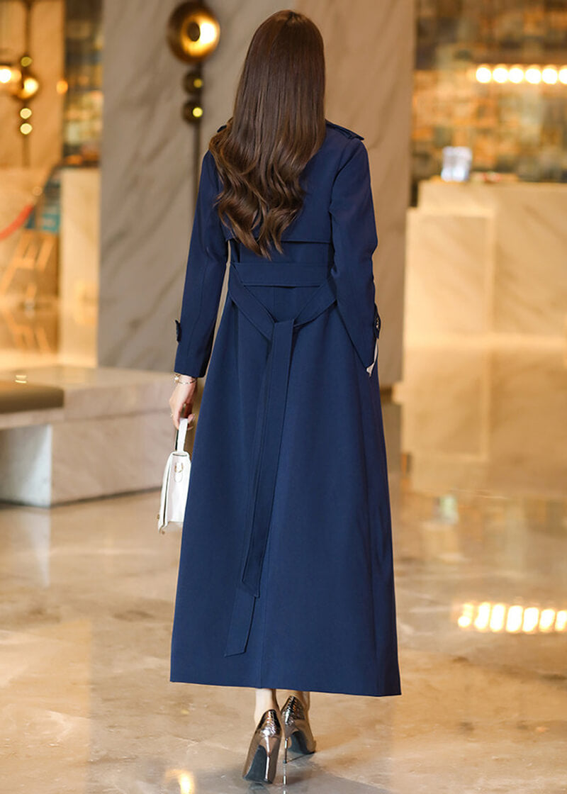 Back view of the belted Vivian Seven long trench coat, emphasizing the professional tailoring and the elegant drape of the navy blue material as the model walks.
