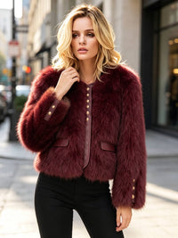 A woman modeling a short, plush faux-fur jacket in deep burgundy with gold-tone decorative buttons, standing on a city street.