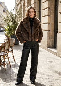 Full-body shot of a woman in an espresso brown plush faux fur crop coat styled with straight-leg leather pants on a city street.