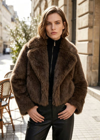 Front view of a woman posing with hands in pockets wearing a short espresso brown faux fur jacket over a black zip turtleneck.