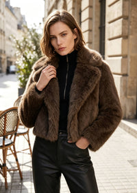 Three-quarter view of a model wearing a tailored espresso brown notch lapel cropped faux fur jacket holding the collar.