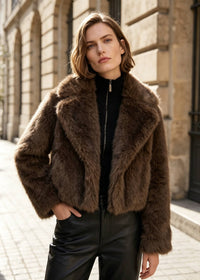 Relaxed street style pose showing the cropped hem and lapel detail of an espresso brown faux fur outerwear jacket for women.