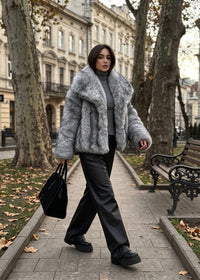 Woman walking outdoors wearing a chunky gray faux fur cropped coat paired with loose black trousers and lug-sole boots