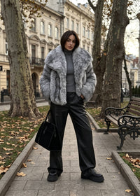 Front view of a chic woman posing on a city walkway in a textured gray faux fur boxy jacket and wide-leg leather pants