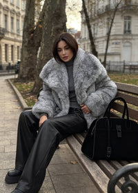 Woman seated on a park bench wearing an exaggerated spread collar gray faux fur jacket paired with chunky black boots