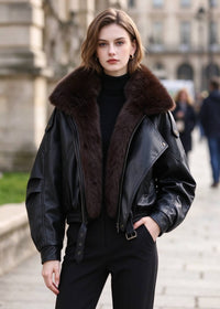 Model posing outdoors wearing black faux leather jacket with dark brown faux fur collar and black trousers.