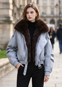 Front view of model with hands in pockets wearing light blue faux leather jacket with faux fur collar.