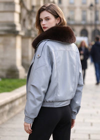 Back view of model wearing light blue faux leather biker jacket with elastic hem and brown fur collar.