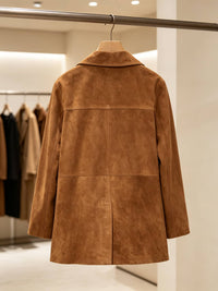 A tan-brown suede jacket hanging on a wooden hanger from a metal clothing rack inside a boutique.