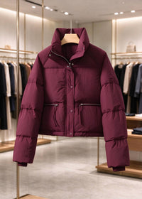 A plum-colored puffer jacket hanging on a wooden hanger inside a modern clothing boutique.