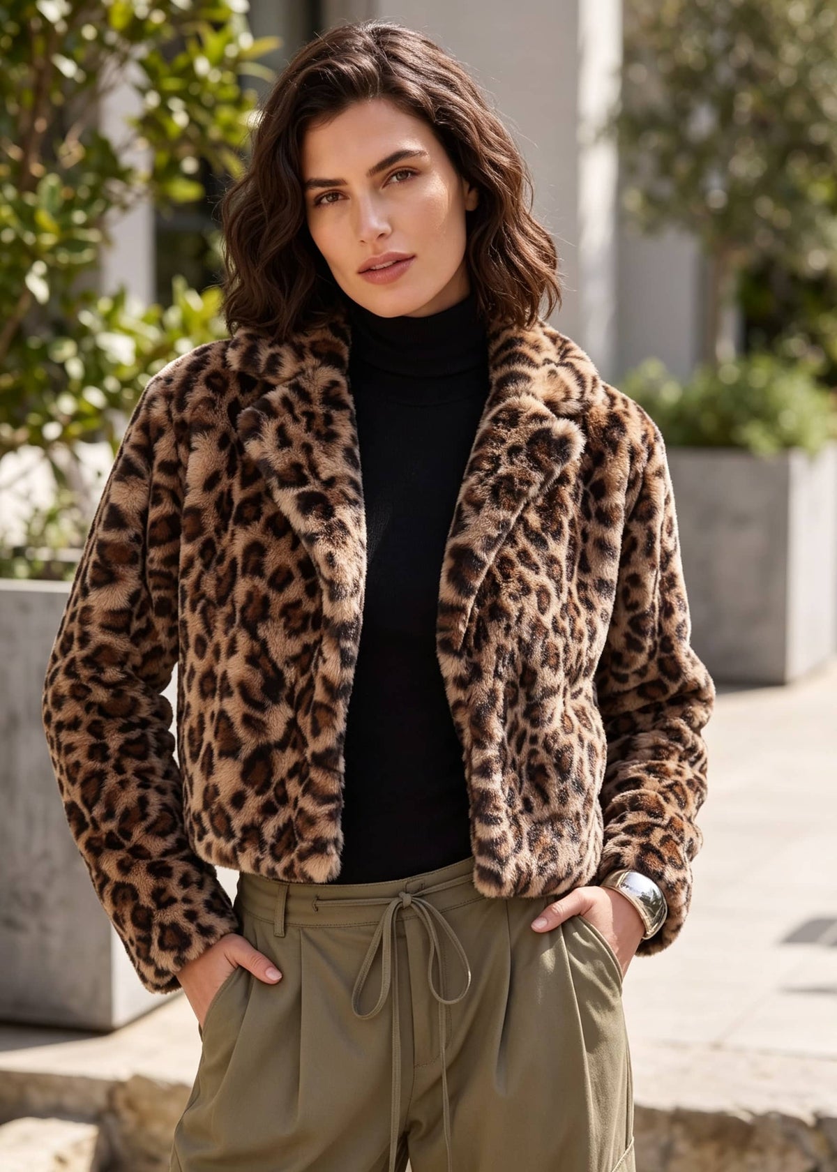 A woman wearing a brown and black leopard-print faux fur jacket over a black turtleneck and olive green drawstring pants, standing outdoors.
