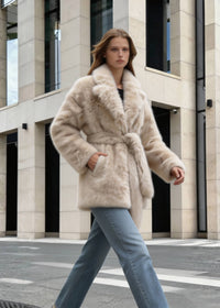 Side view of a model walking in a luxury cream faux fur wrap coat styled with straight-leg denim jeans.