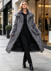 Full-length front view of a model presenting a charcoal grey longline shaggy faux fur coat worn open over an all-black tailored outfit.
