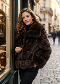 Outdoor shopfront portrait of a woman standing by a cafe window wearing a warm brown paneled faux fur cropped jacket