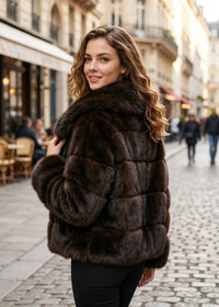 Over-the-shoulder back view of a woman showing the horizontal paneled construction of an espresso brown faux fur cropped jacket