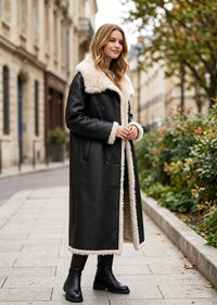 Three-quarter side angle of a woman wearing a black leather and shearling double-breasted longline winter coat.