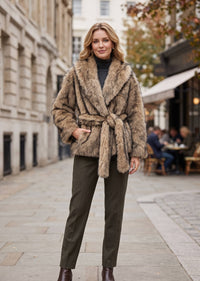 Full-length shot of a woman modeling a belted caramel faux fur wrap coat with straight-leg pants on a city street
