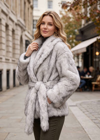 Smiling woman outdoors wearing a light silver gray faux fur wrap jacket tied with a matching self-belt