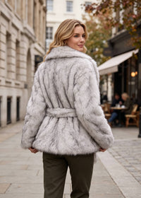 Back view of a woman showing the fit and belted waist of a plush silver-gray faux fur winter coat