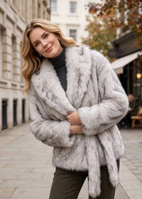 Close-up street style shot of a blonde woman wearing a belted light gray faux fur short coat with a shawl collar