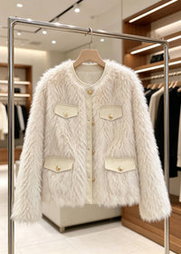 A cream faux fur jacket with beige panels and gold buttons, hanging on a clothing rack inside a boutique.
