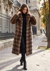 Full-length front view of a woman walking outdoors wearing a brown tiered faux fur long coat with a wide wing collar