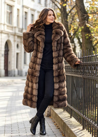 Outdoor full shot of a woman leaning against an ornate iron fence wearing a cozy brown tiered faux fur longline coat