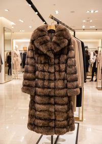 Studio retail hanger display of a women's luxury brown tiered wing collar faux fur long coat on a rack