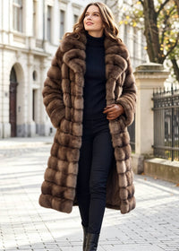 Full body front angle of a smiling woman strolling outdoors in an oversized brown horizontal paneled faux fur long coat