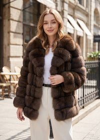 Front-facing portrait of a woman modeling a plush brown tiered faux fur car coat with a wide wing collar on a sunny street
