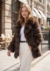 Walking street view of a woman in an elegant espresso brown tiered faux fur mid-length coat paired with high-waisted white pants